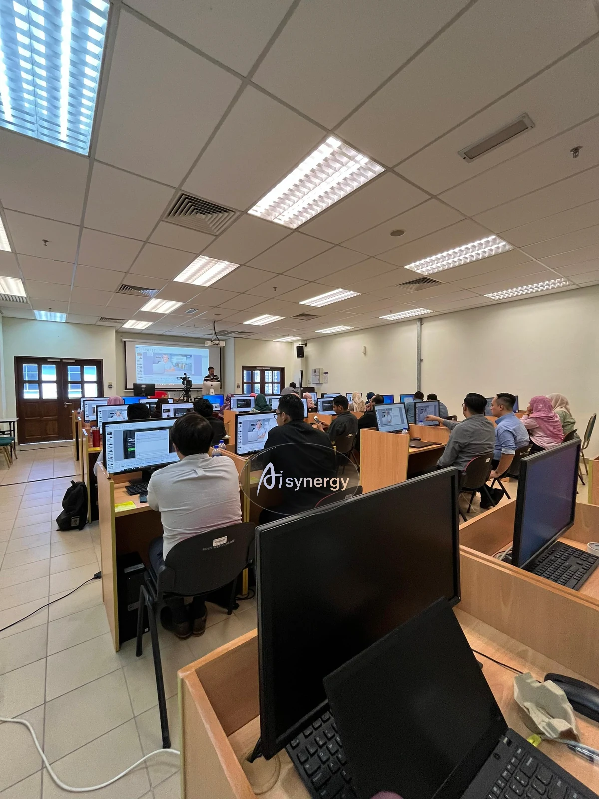 Wide view of a computer-lab training session with participants following along on their own screens