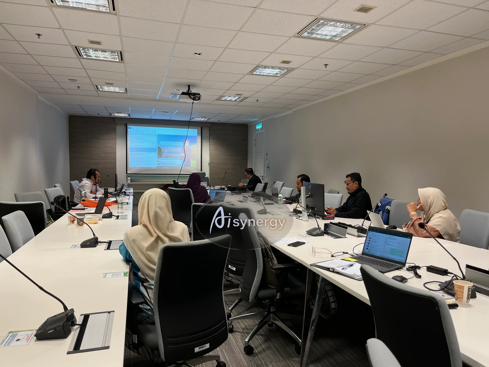 A boardroom-style training session with participants seated around a long table facing a presentation screen