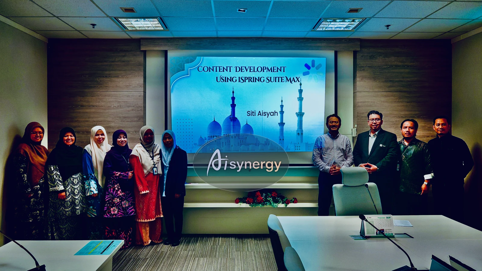 Trainer and a group of participants posing together in front of a presentation screen at the end of a session