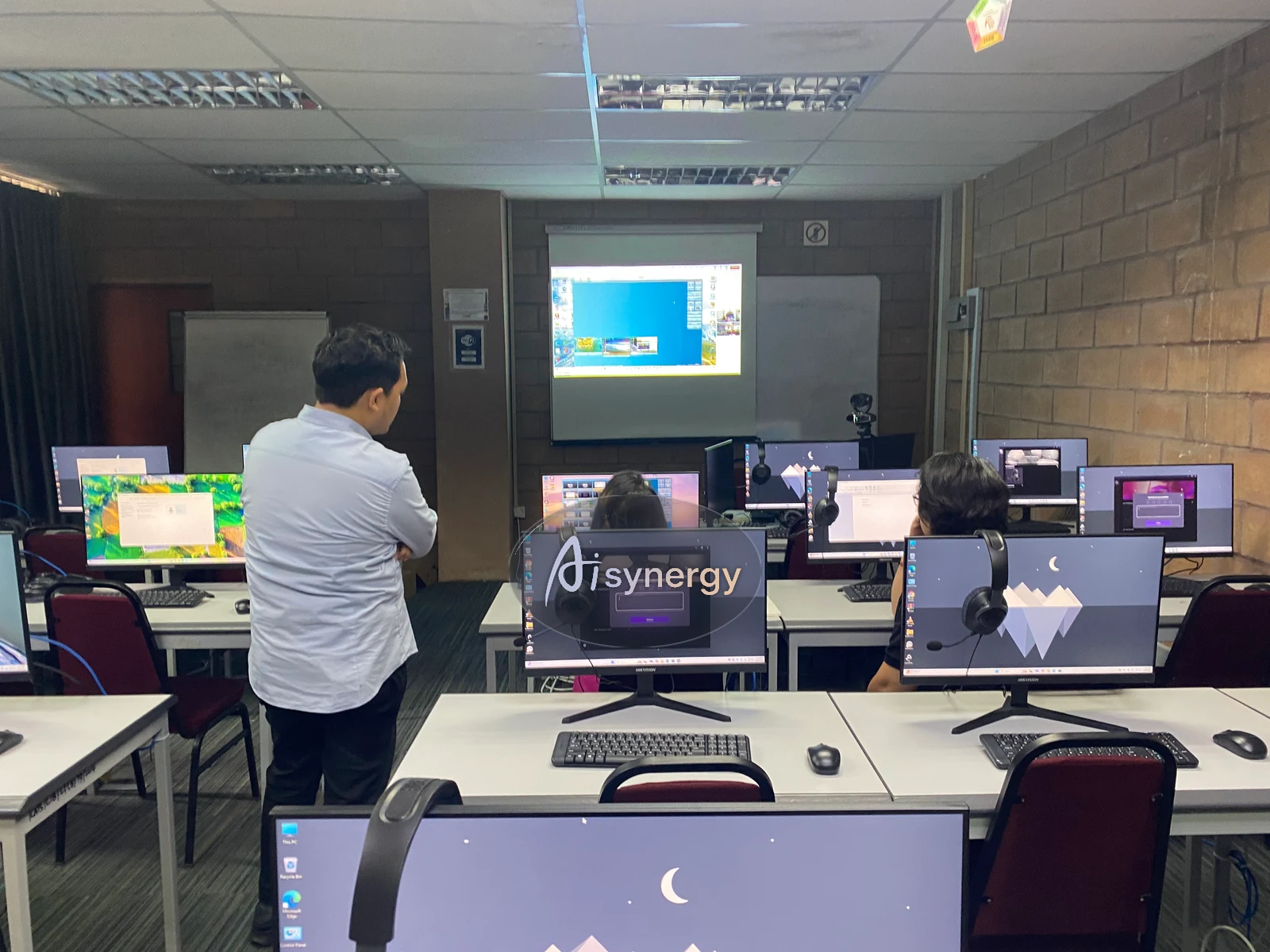 Wide view of a hands-on computer-lab session with a trainer reviewing participants’ builds