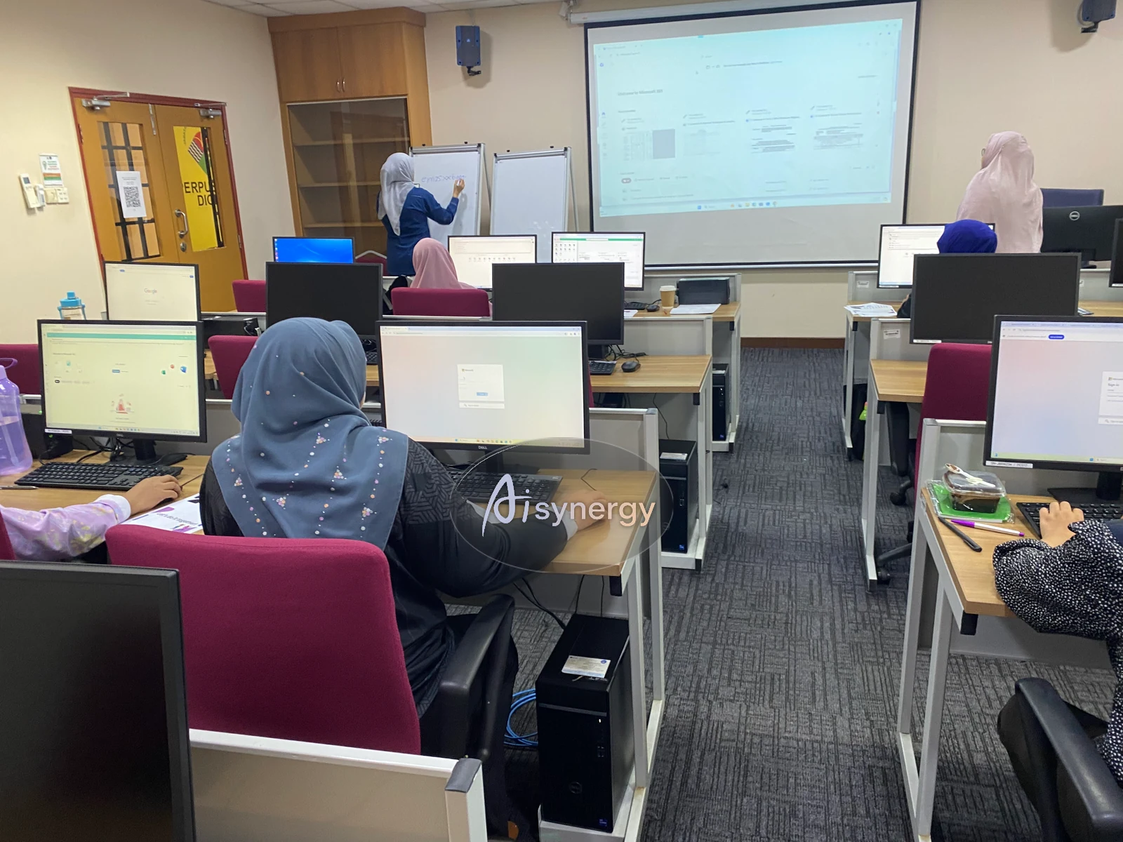 Wide view of a computer-lab training session with participants following along on their own screens
